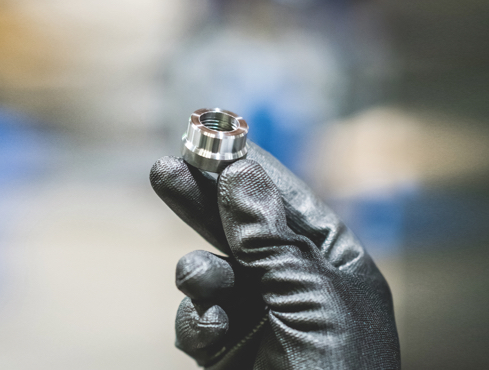 A person is holding a bolt between 3 fingers. They are also wearing thick gloves.