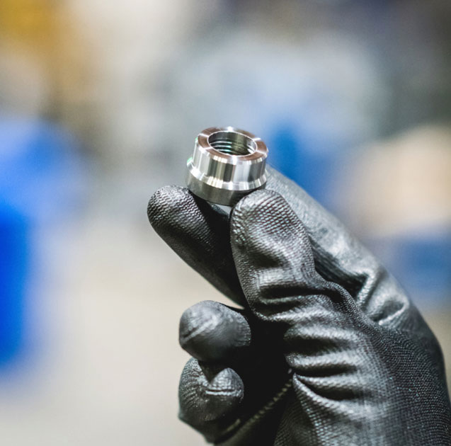 A person is holding a bolt between 3 fingers. They are also wearing thick gloves.