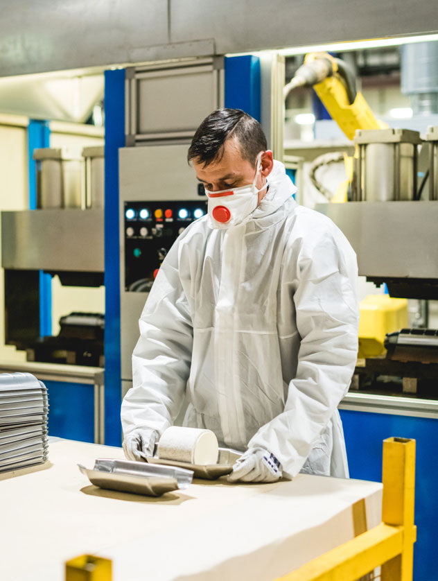A factory worker is in a paper suit and mask as he works on a product part
