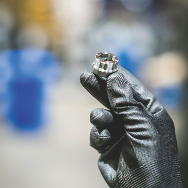 A person is holding a bolt between 3 fingers. They are also wearing thick gloves.