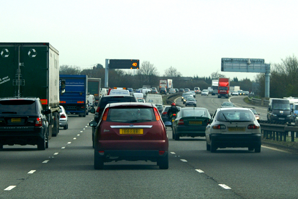 There are cars driving through traffic on the motorway. The speed sign in the distance is displaying the number "40" and there are cars in all 3 lanes.
