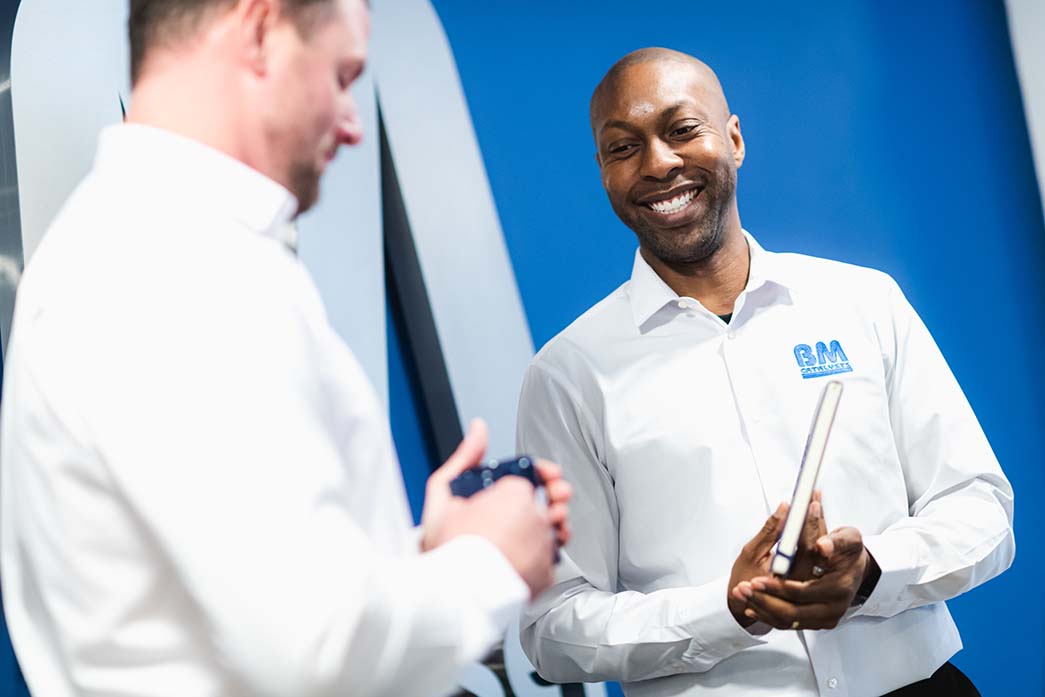 Two BM Catalyst workers are interacting. One of the men is smiling and holding a notebook while the other is hold a coffee mug.