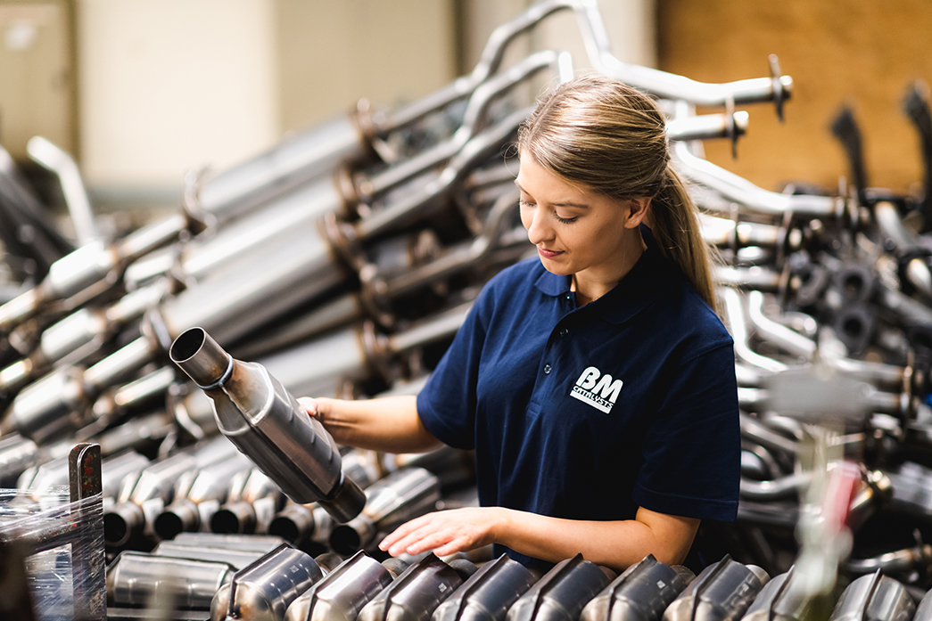 A woman is sorting through car parts in a manufacturing facility. 